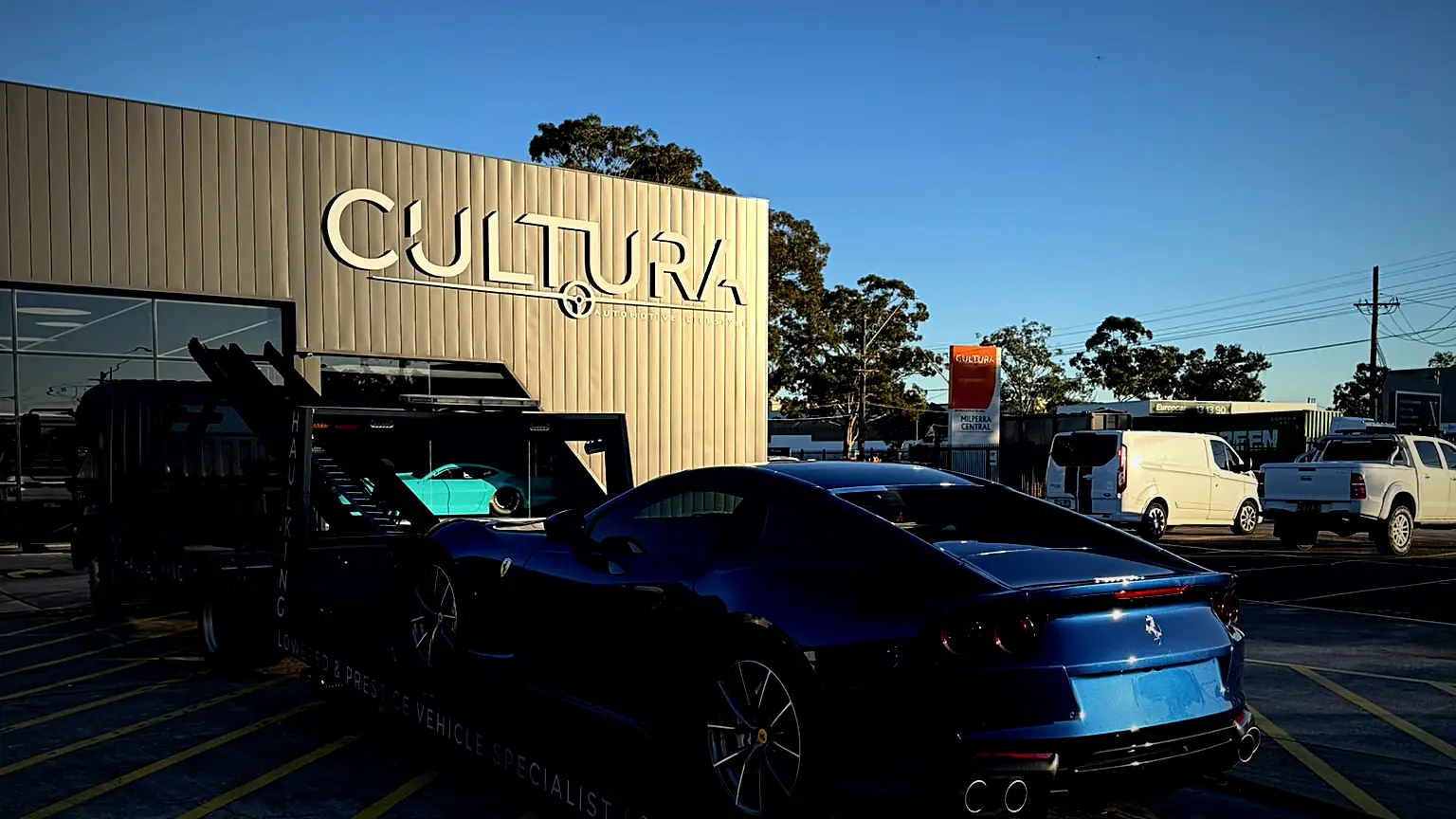 Blue Ferrari 812 on HaulKing's tray at Cultura Automotive in golden-hour light